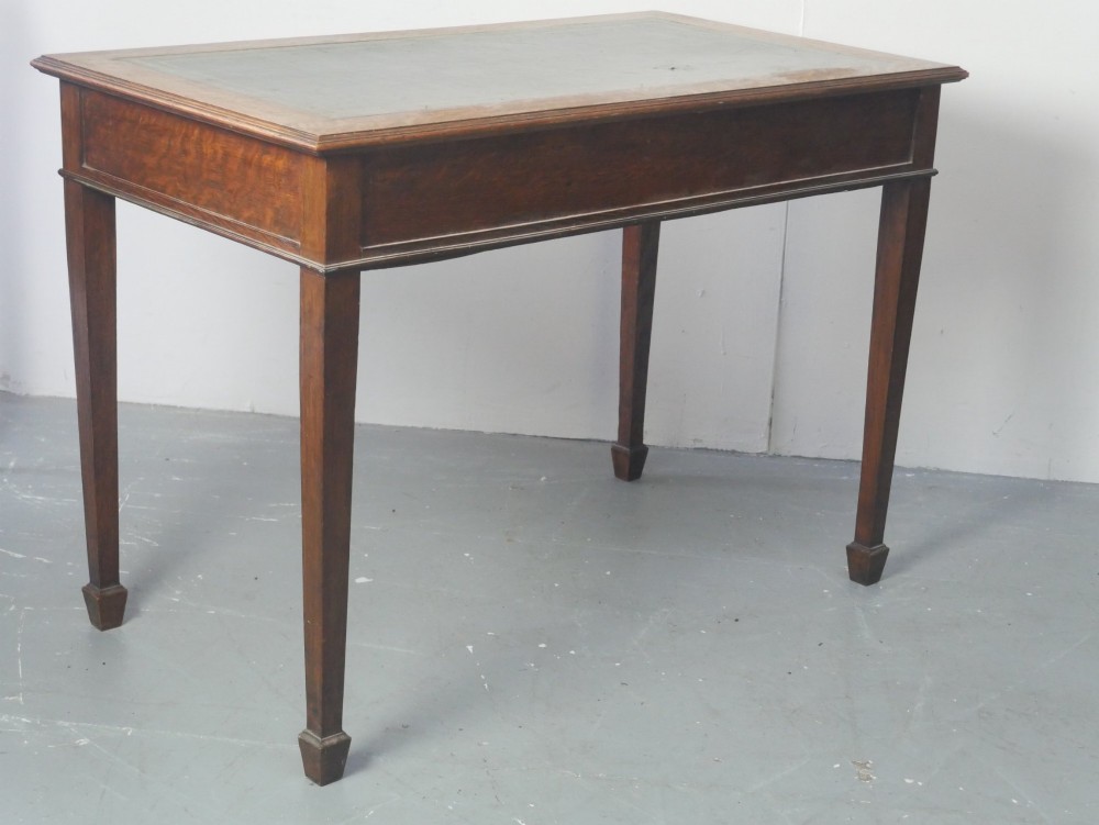 A warm brown oak writing desk with two drawer fronts featuring brass drop handles, resting on four square tapered legs. View VIII