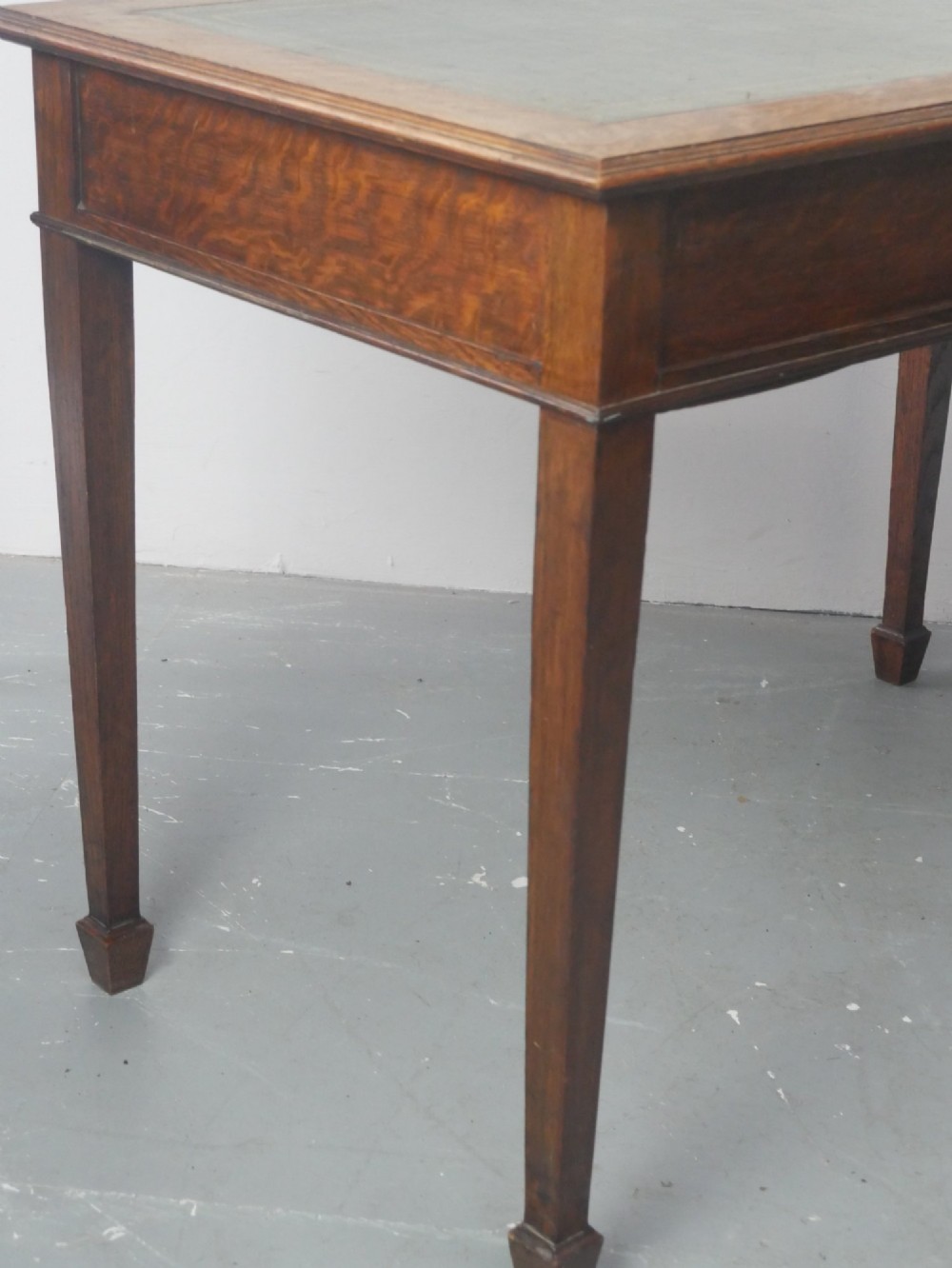 A warm brown oak writing desk with two drawer fronts featuring brass drop handles, resting on four square tapered legs. View IX