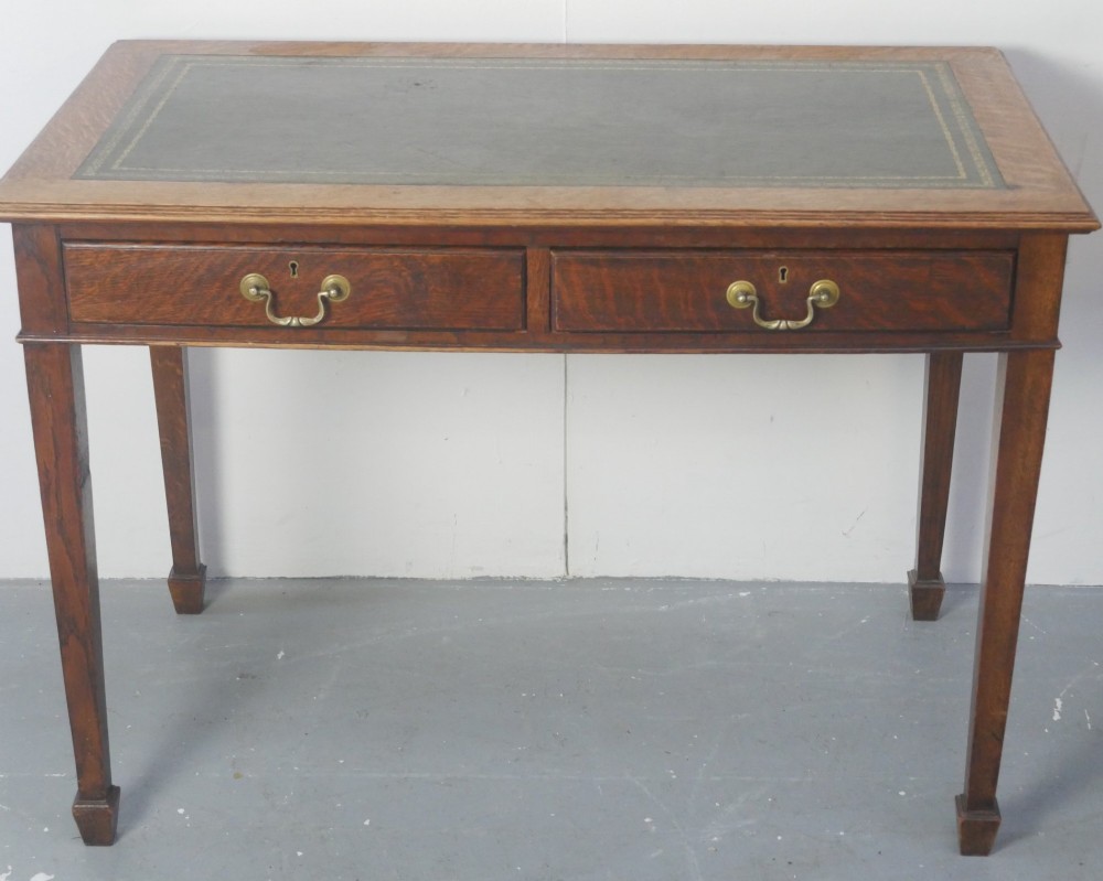 A warm brown oak writing desk with two drawer fronts featuring brass drop handles, resting on four square tapered legs. View XIII