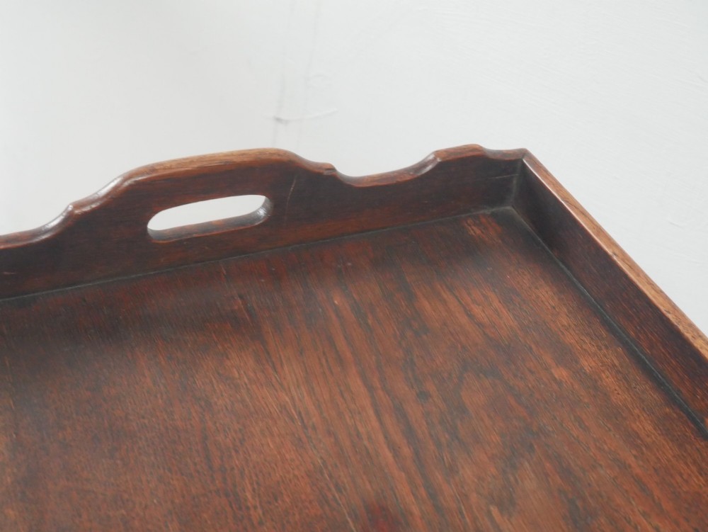 A dark oak butler tray with gallery edges and cut-out handles resting atop a matching wooden folding X-frame stand with turned legs. View IV