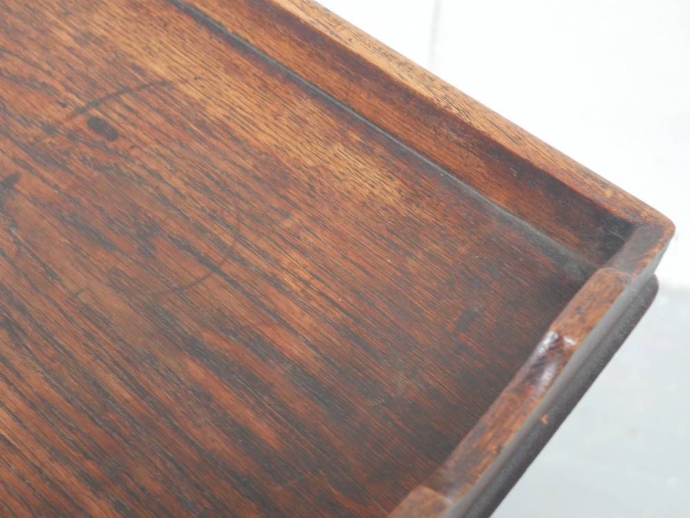 A dark oak butler tray with gallery edges and cut-out handles resting atop a matching wooden folding X-frame stand with turned legs. View V