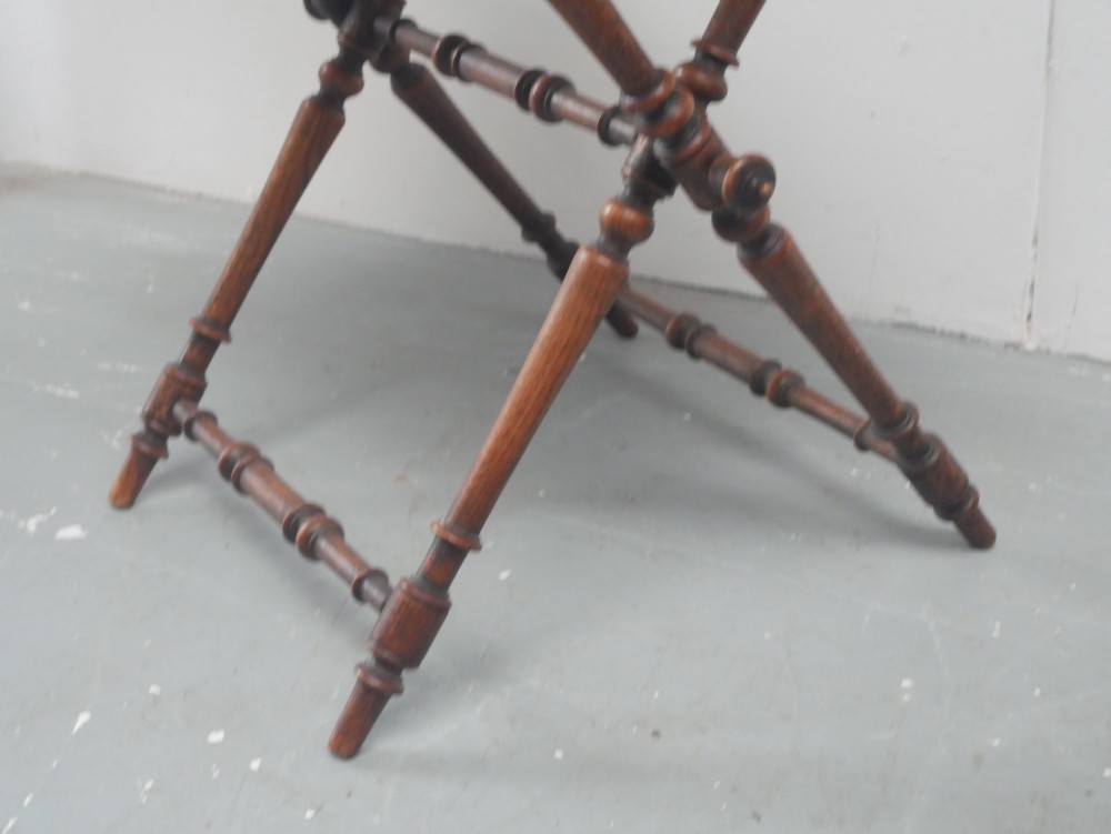 A dark oak butler tray with gallery edges and cut-out handles resting atop a matching wooden folding X-frame stand with turned legs. View VII