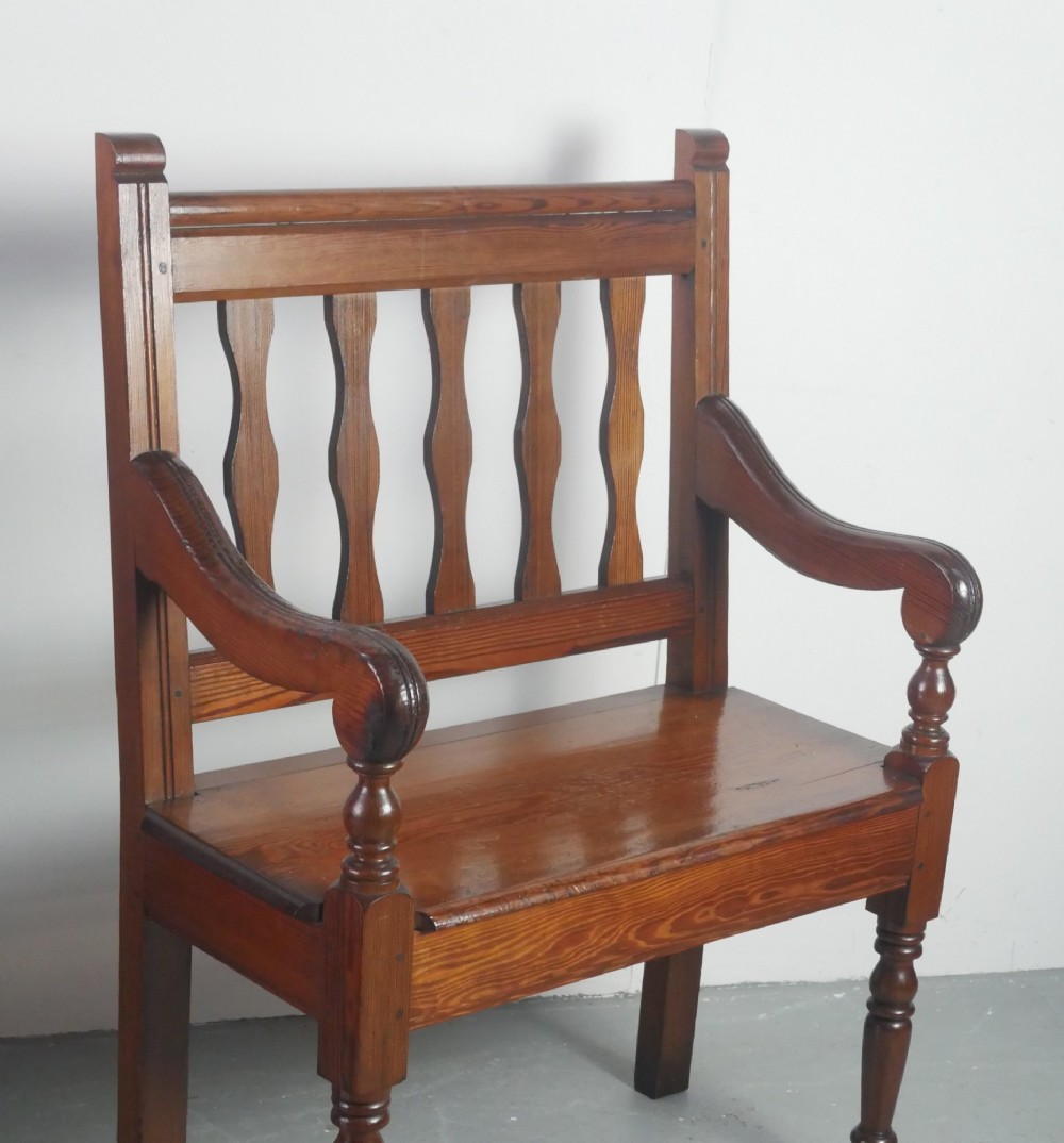A warm brown pine hall bench featuring turned front legs, shaped back slats, swept armrests, and a solid timber seat. View VI