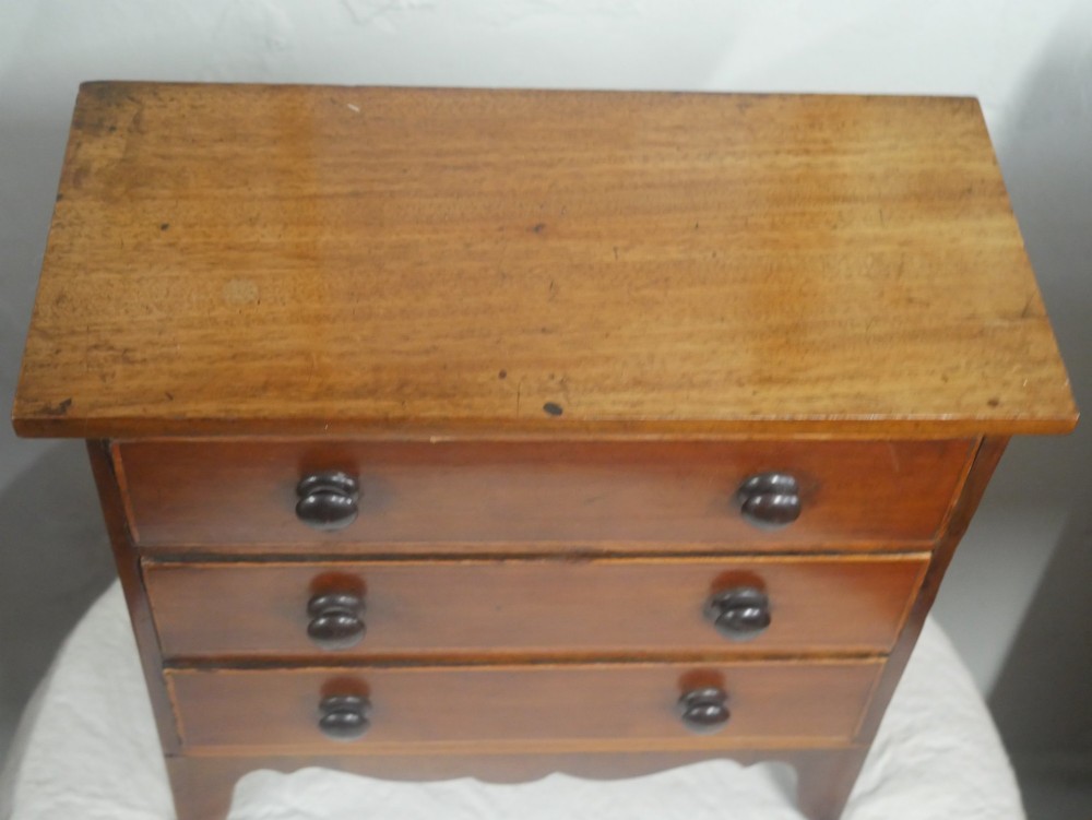 A miniature warm brown wooden chest of drawers featuring three graduated drawers with round knobs and a scalloped lower apron. View II