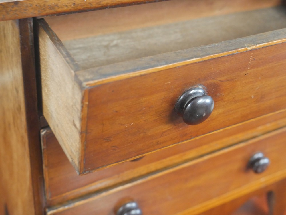 A miniature warm brown wooden chest of drawers featuring three graduated drawers with round knobs and a scalloped lower apron. View VIII
