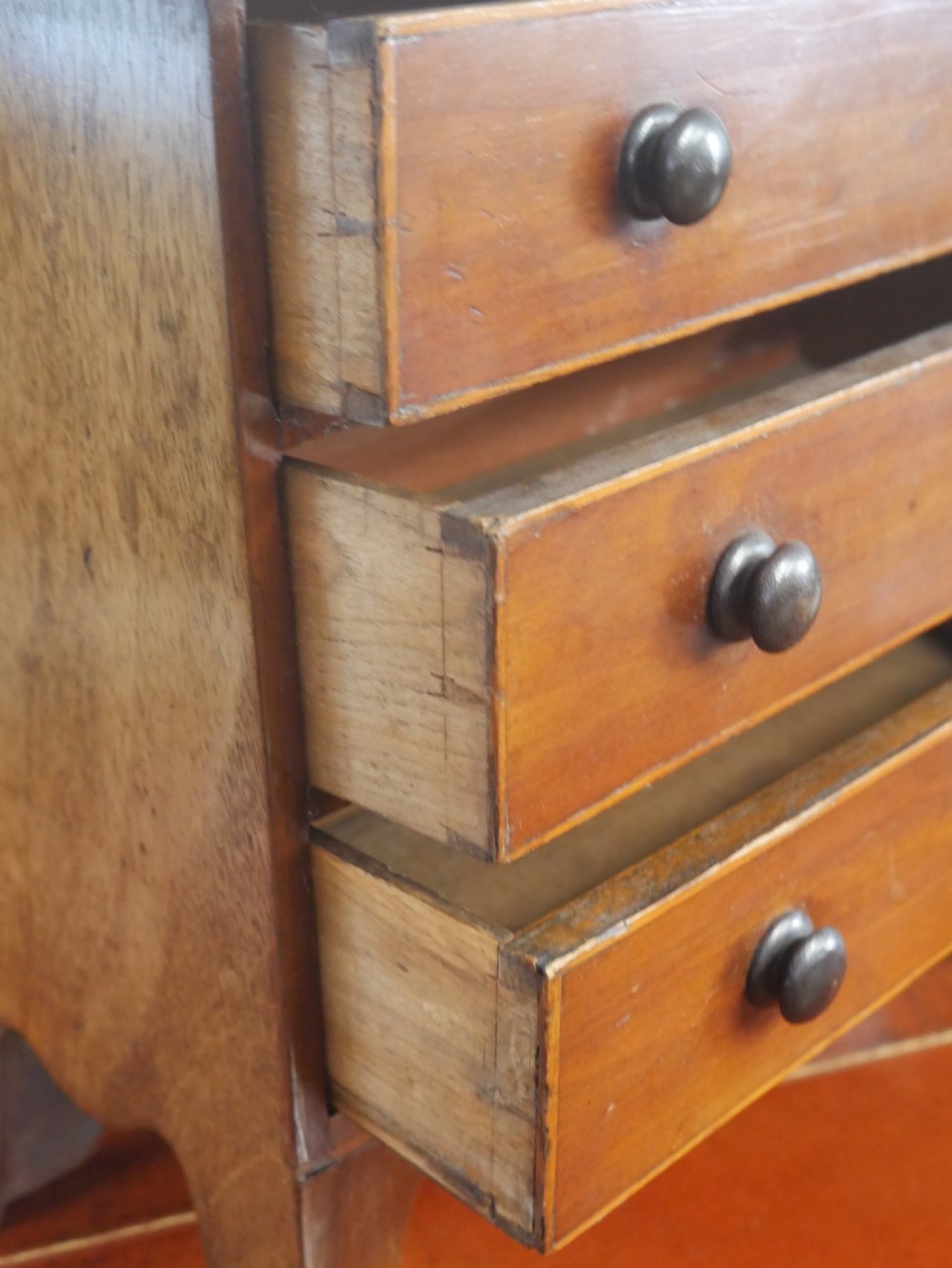 A miniature warm brown wooden chest of drawers featuring three graduated drawers with round knobs and a scalloped lower apron. View IX