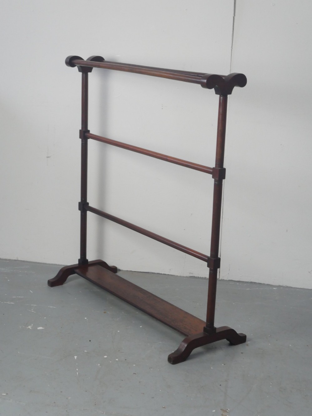 A dark mahogany freestanding towel rail featuring scrolled top terminals, turned vertical posts, and multiple horizontal drying bars supported on sledge feet.