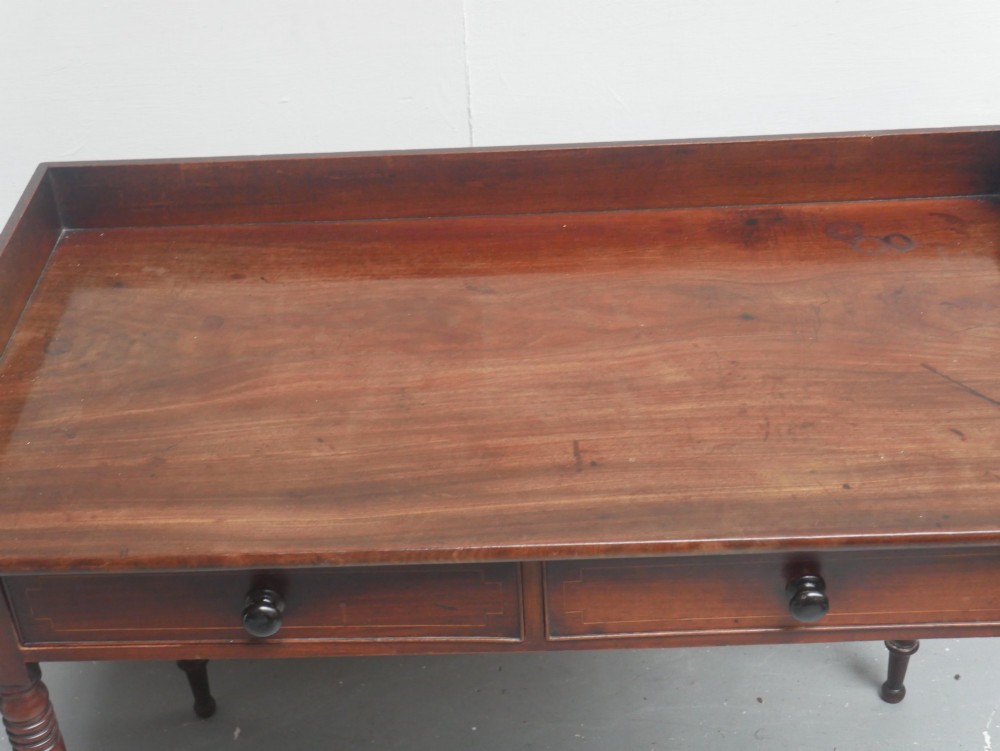 An antique Regency mahogany writing table featuring a raised gallery back, two frieze drawers with line inlay, and turned legs. View VI