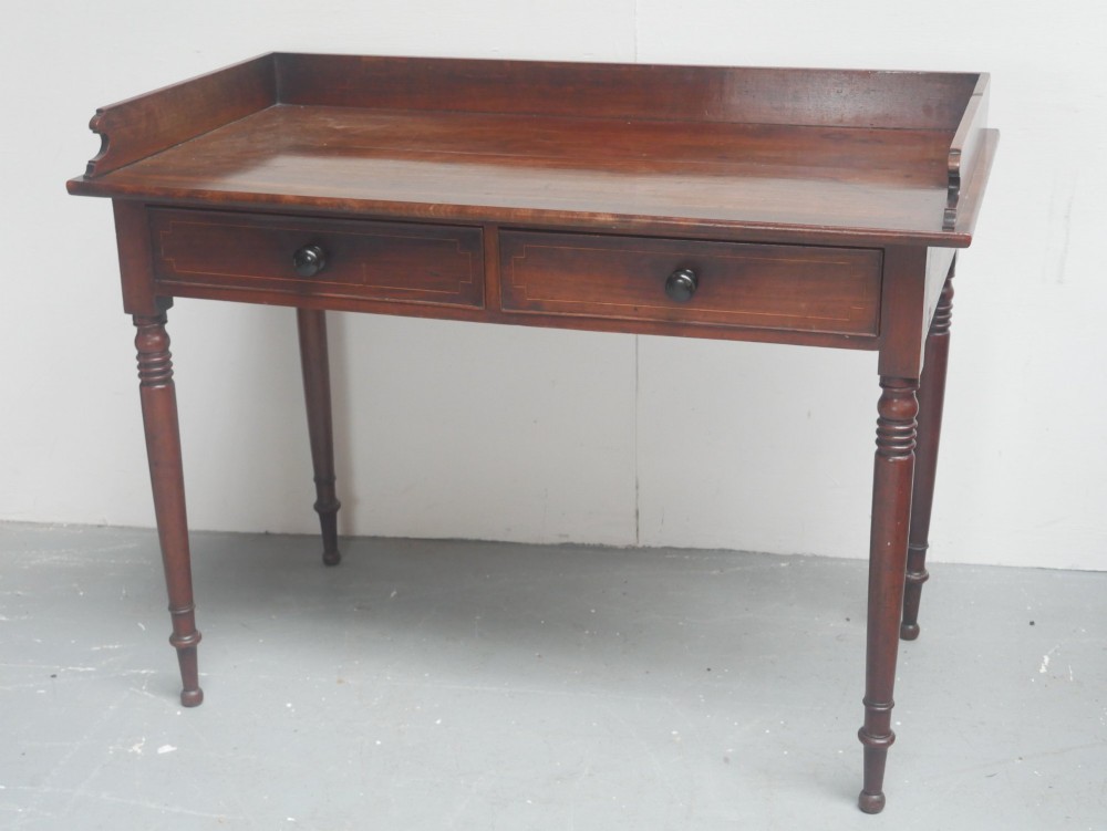 An antique Regency mahogany writing table featuring a raised gallery back, two frieze drawers with line inlay, and turned legs. View X
