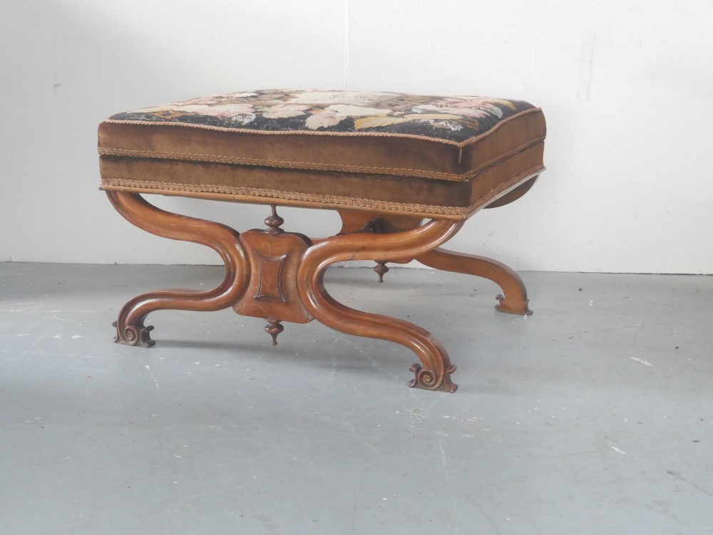 An antique Scottish Baronial X-frame stool crafted from carved wood with scrolled feet, turned finials, and a brown velvet seat with floral tapestry top.