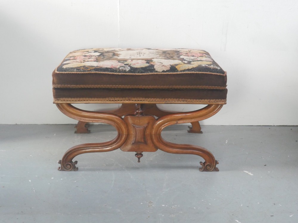 An antique Scottish Baronial X-frame stool crafted from carved wood with scrolled feet, turned finials, and a brown velvet seat with floral tapestry top. View II