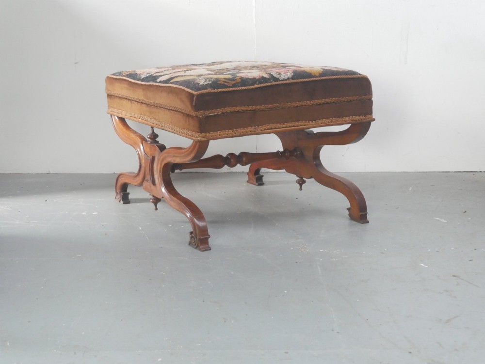 An antique Scottish Baronial X-frame stool crafted from carved wood with scrolled feet, turned finials, and a brown velvet seat with floral tapestry top. View VI