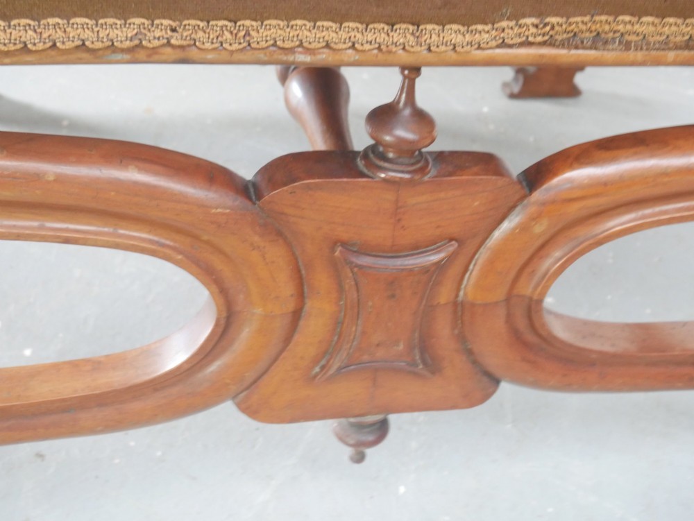 An antique Scottish Baronial X-frame stool crafted from carved wood with scrolled feet, turned finials, and a brown velvet seat with floral tapestry top. View VII