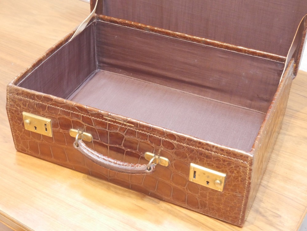 A small warm brown crocodile skin suitcase with brass locks and a stitched leather handle. View III