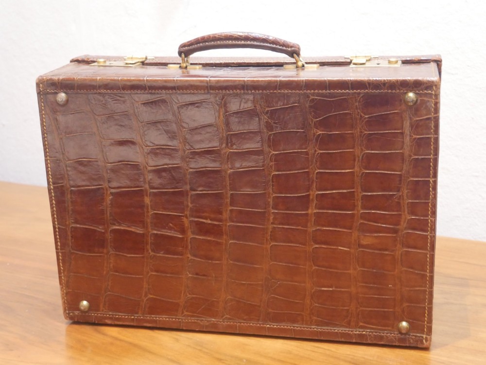 A small warm brown crocodile skin suitcase with brass locks and a stitched leather handle. View VI