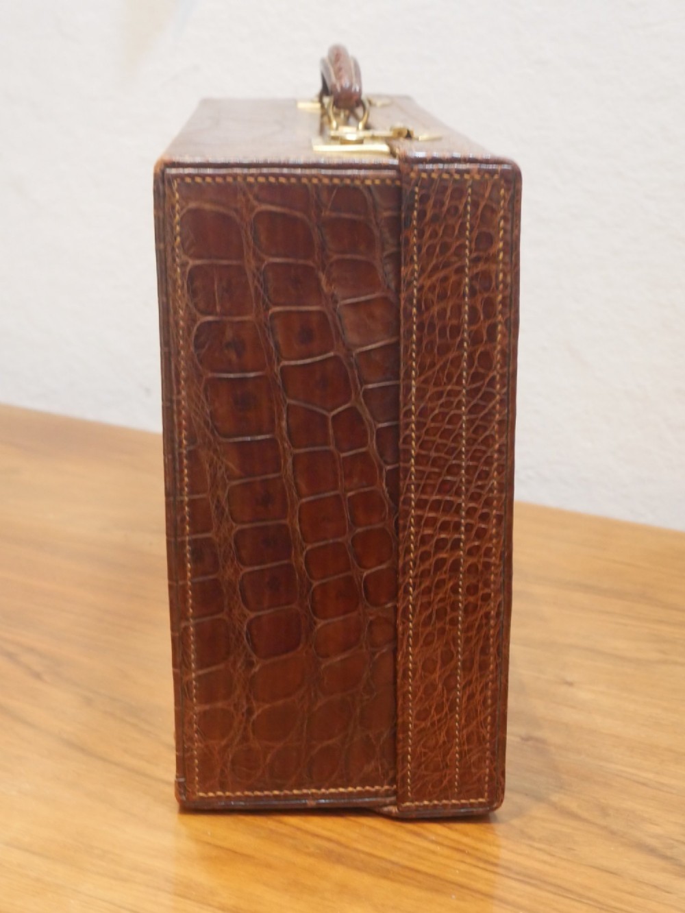 A small warm brown crocodile skin suitcase with brass locks and a stitched leather handle. View VII