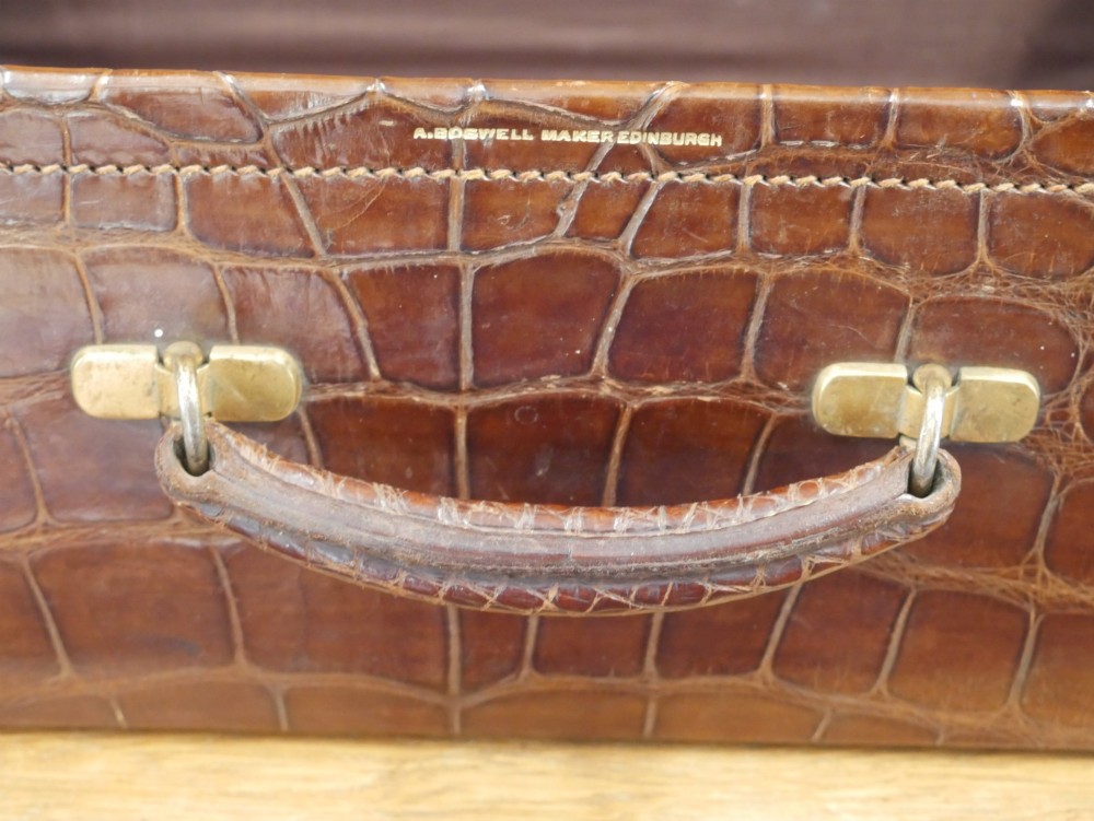 A small warm brown crocodile skin suitcase with brass locks and a stitched leather handle. View X