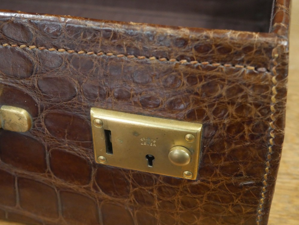 A small warm brown crocodile skin suitcase with brass locks and a stitched leather handle. View XI