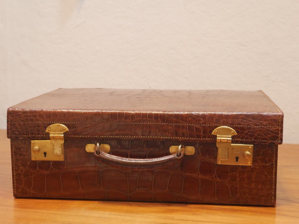 A small warm brown crocodile skin suitcase with brass locks and a stitched leather handle. View XII