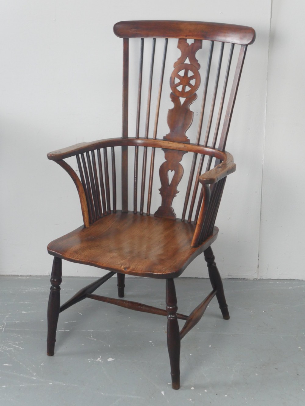 A warm brown antique Windsor armchair featuring a high back with a pierced wheelback splat, curved arms, and turned wooden legs.