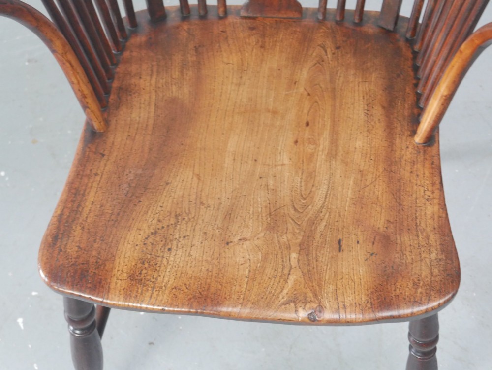 A warm brown antique Windsor armchair featuring a high back with a pierced wheelback splat, curved arms, and turned wooden legs. View V