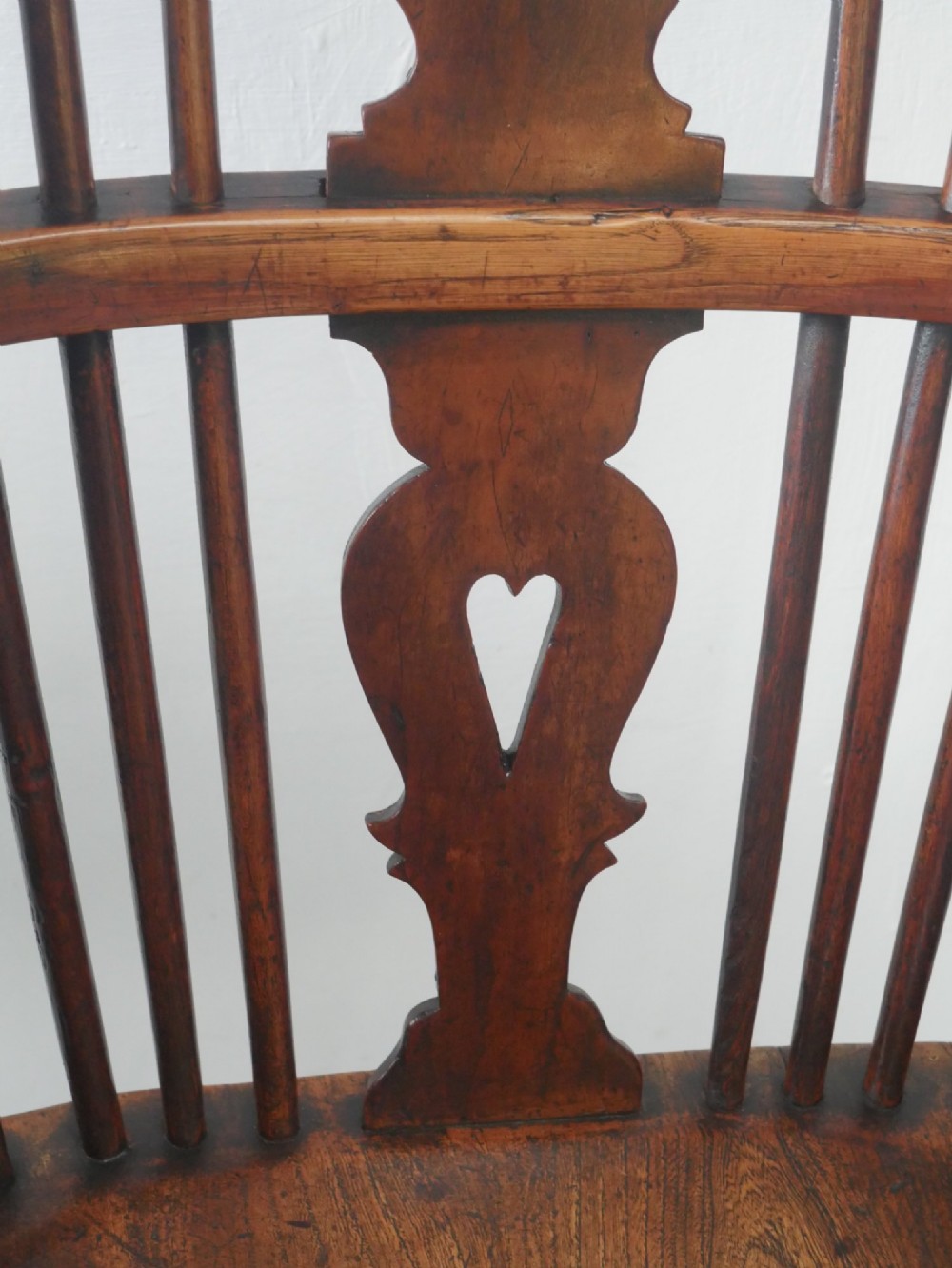A warm brown antique Windsor armchair featuring a high back with a pierced wheelback splat, curved arms, and turned wooden legs. View X