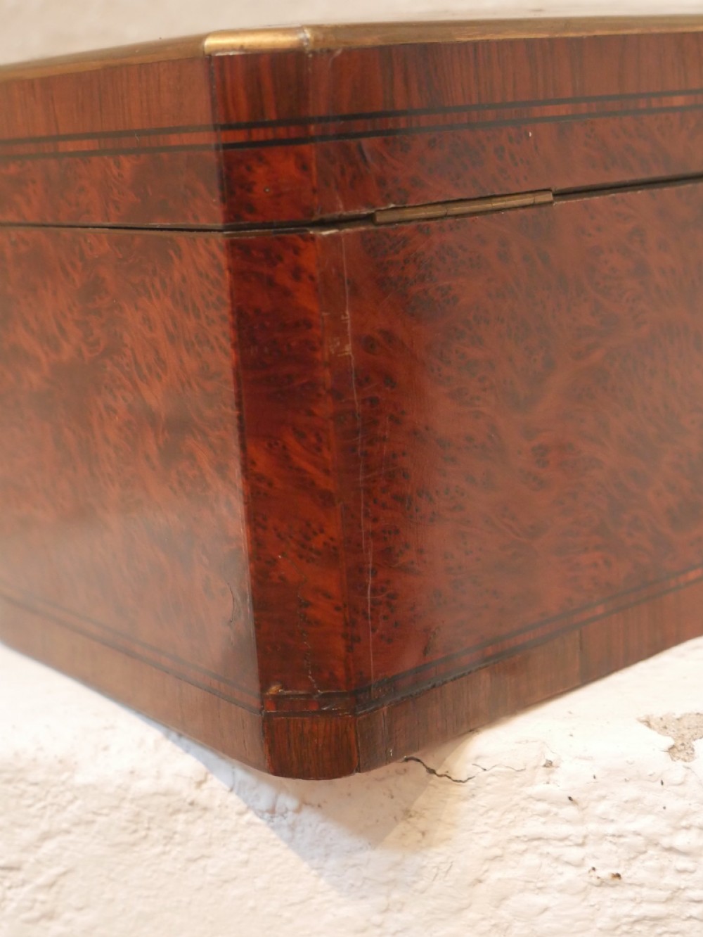 A 19th-century French amboyna wood box featuring canted corners, brass edging, and central brass inlay on the lid. View X