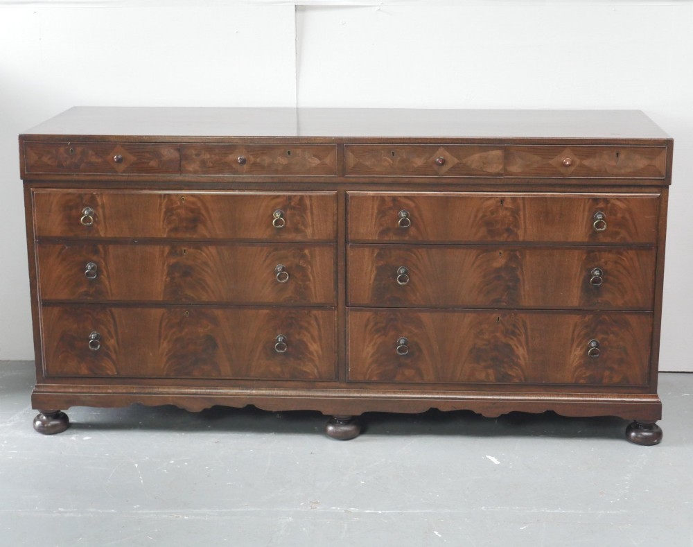 A wide Scottish flame mahogany chest of drawers featuring top diamond-inlaid frieze drawers, brass drop handles, and turned feet.