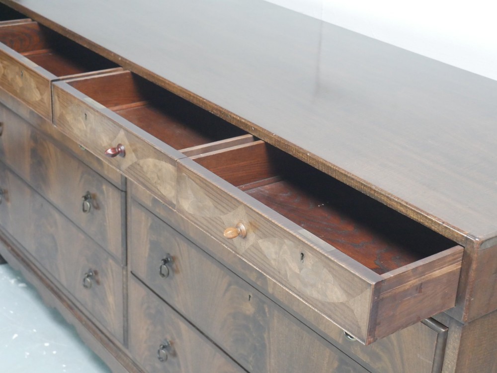 A wide Scottish flame mahogany chest of drawers featuring top diamond-inlaid frieze drawers, brass drop handles, and turned feet. View II