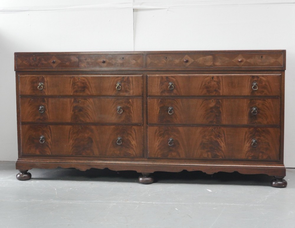 A wide Scottish flame mahogany chest of drawers featuring top diamond-inlaid frieze drawers, brass drop handles, and turned feet. View X