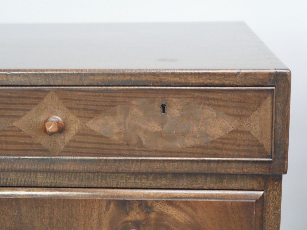 A wide Scottish flame mahogany chest of drawers featuring top diamond-inlaid frieze drawers, brass drop handles, and turned feet. View XII