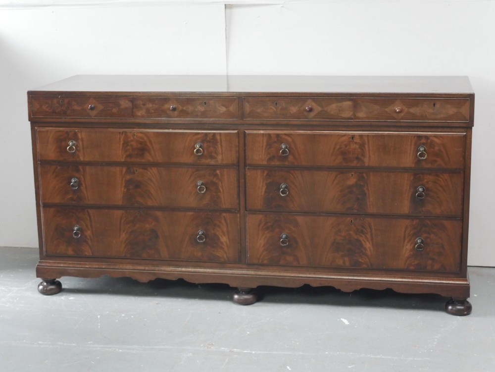 A wide Scottish flame mahogany chest of drawers featuring top diamond-inlaid frieze drawers, brass drop handles, and turned feet. View XV
