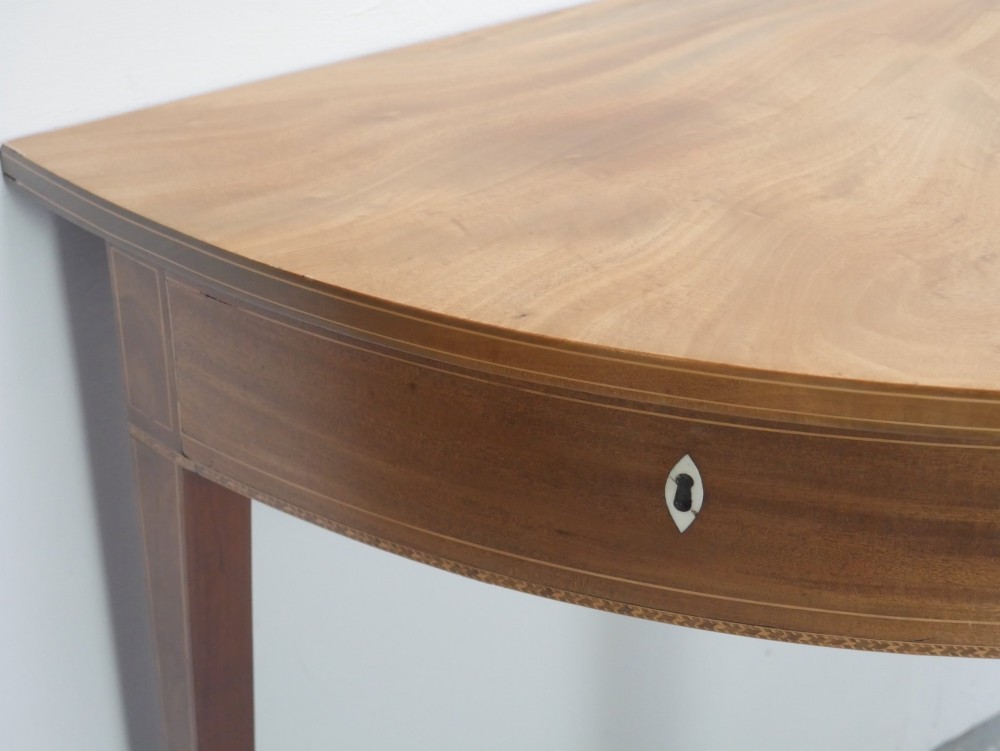 A Regency mahogany demi-lune console table featuring satinwood stringing inlay, a central drawer, and four square tapered legs. View III
