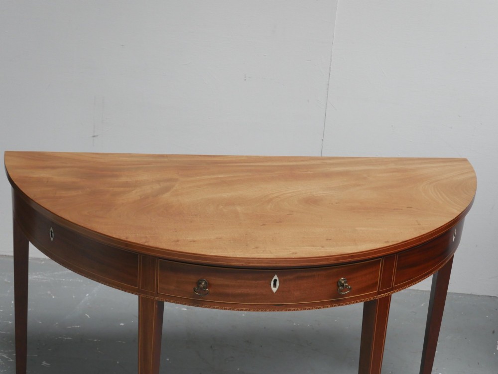 A Regency mahogany demi-lune console table featuring satinwood stringing inlay, a central drawer, and four square tapered legs. View IX