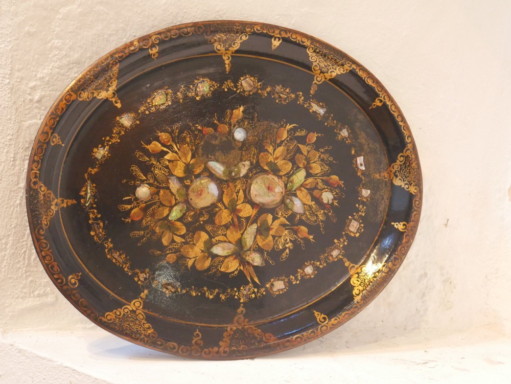 An oval black lacquered papier-mache tray decorated with gilt floral scrollwork and iridescent mother-of-pearl inlay.