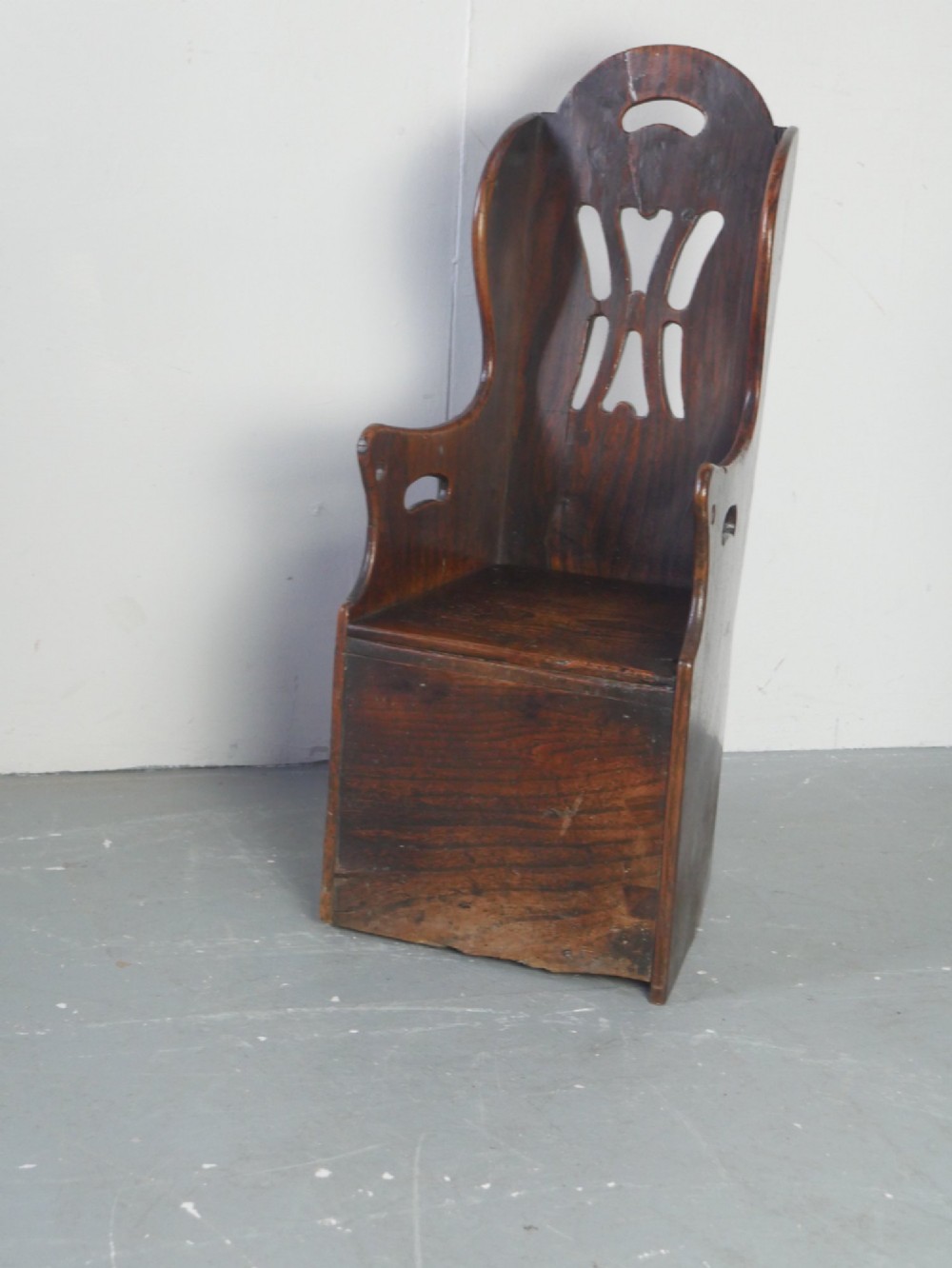 An 18th-century dark oak childs chair featuring a high winged back with decorative pierced cutouts and a solid box base.
