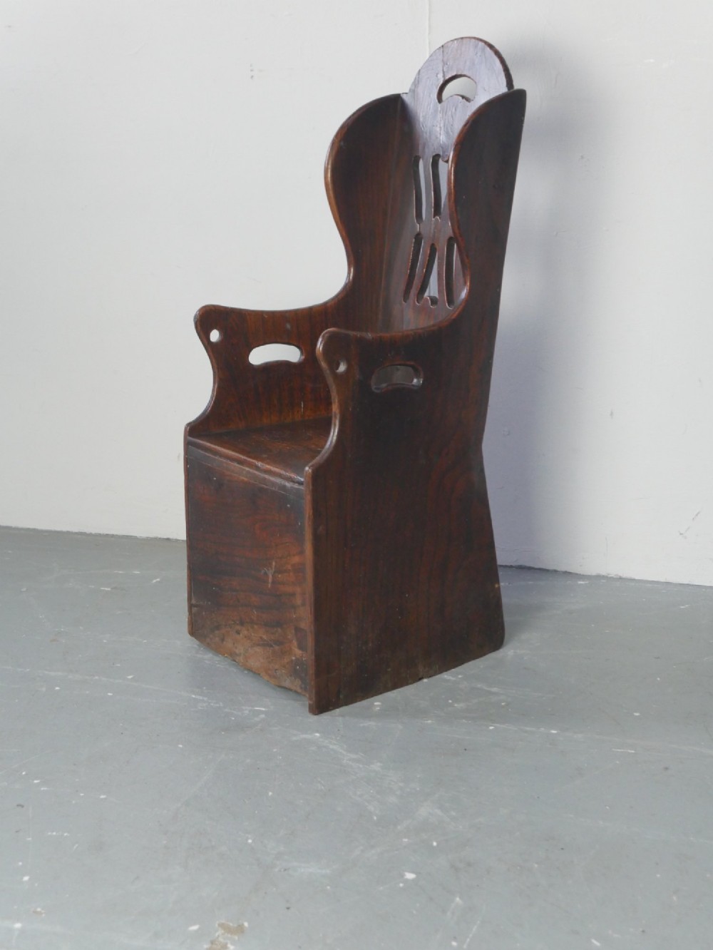 An 18th-century dark oak childs chair featuring a high winged back with decorative pierced cutouts and a solid box base. View II