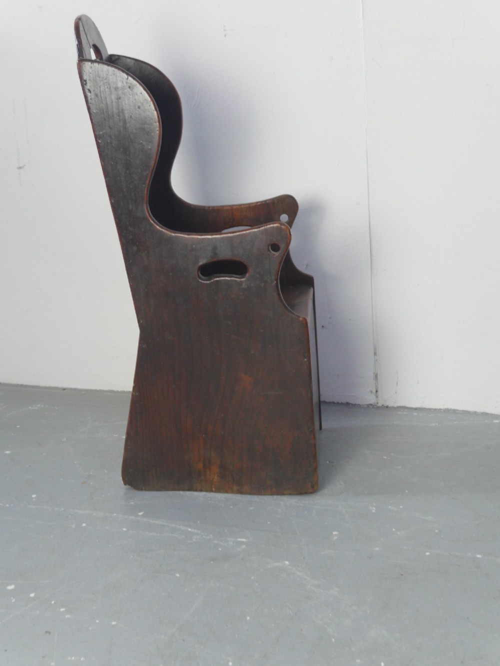 An 18th-century dark oak childs chair featuring a high winged back with decorative pierced cutouts and a solid box base. View III