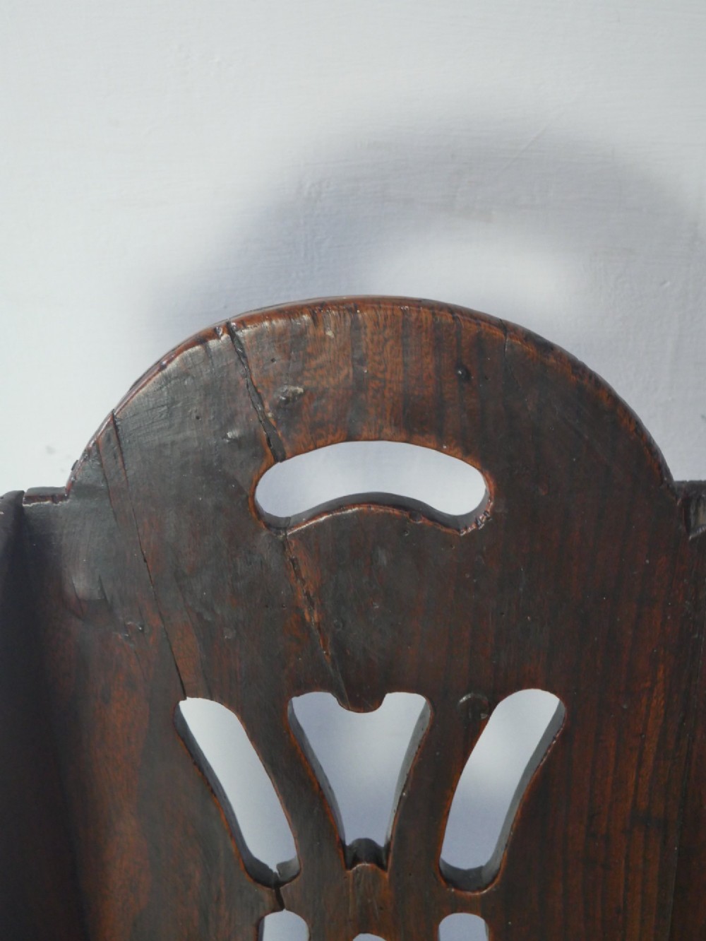 An 18th-century dark oak childs chair featuring a high winged back with decorative pierced cutouts and a solid box base. View V