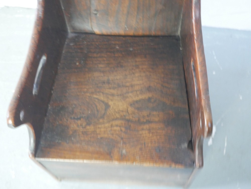 An 18th-century dark oak childs chair featuring a high winged back with decorative pierced cutouts and a solid box base. View VI