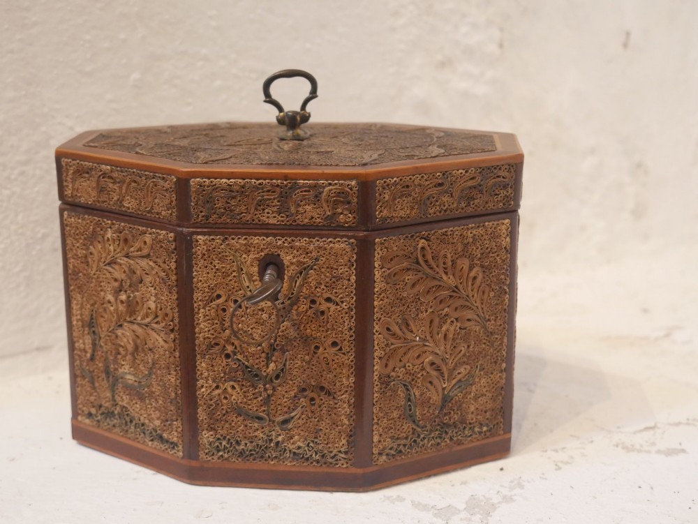 An 18th-century octagonal wooden tea caddy featuring intricate paper filigree quilling, foliate designs, a top brass loop handle, and a key.