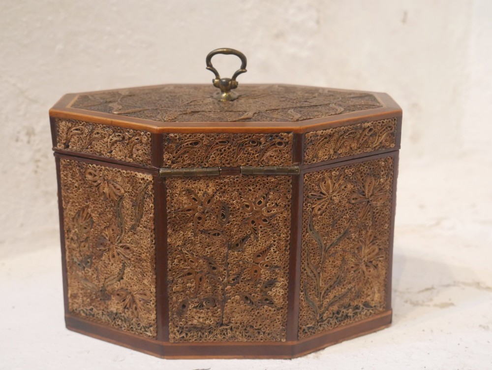 An 18th-century octagonal wooden tea caddy featuring intricate paper filigree quilling, foliate designs, a top brass loop handle, and a key. View VI