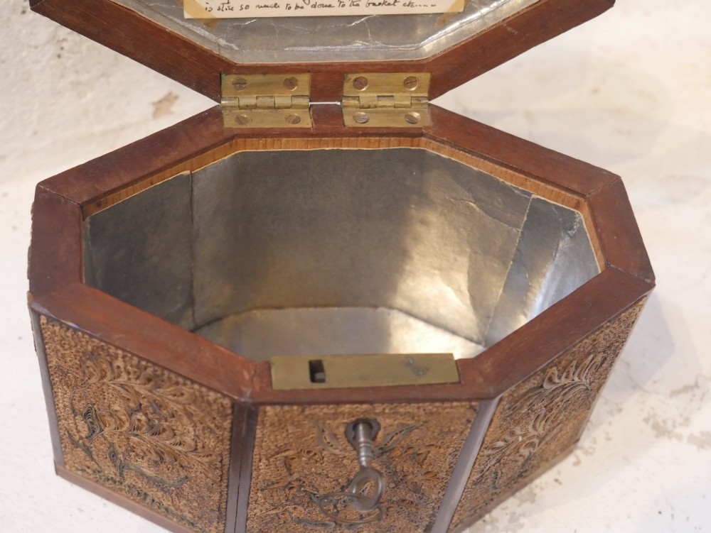An 18th-century octagonal wooden tea caddy featuring intricate paper filigree quilling, foliate designs, a top brass loop handle, and a key. View IX