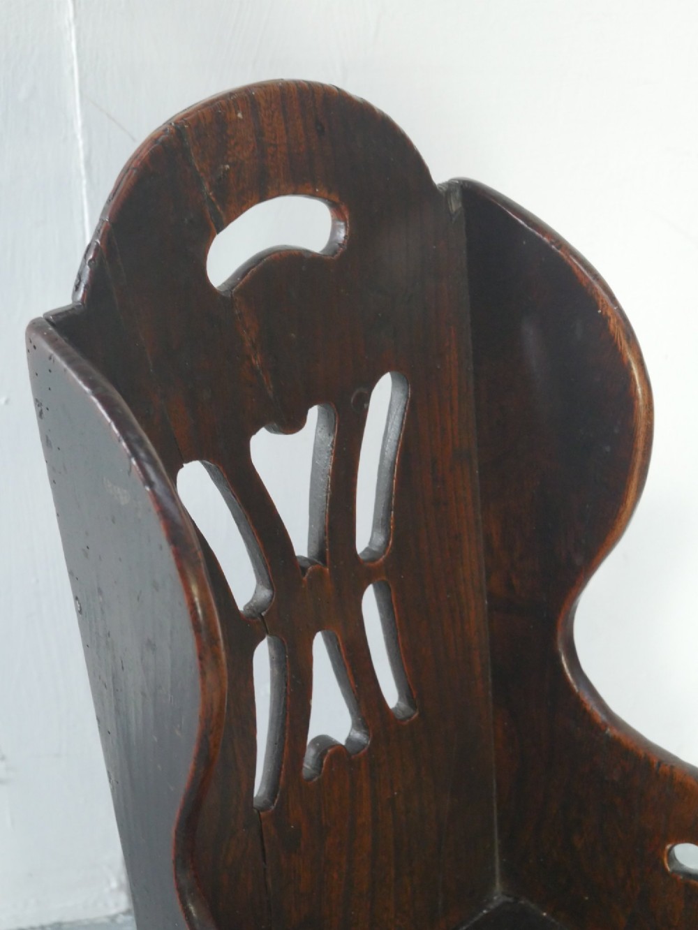 An 18th-century dark oak childs chair featuring a high winged back with decorative pierced cutouts and a solid box base. View XIII