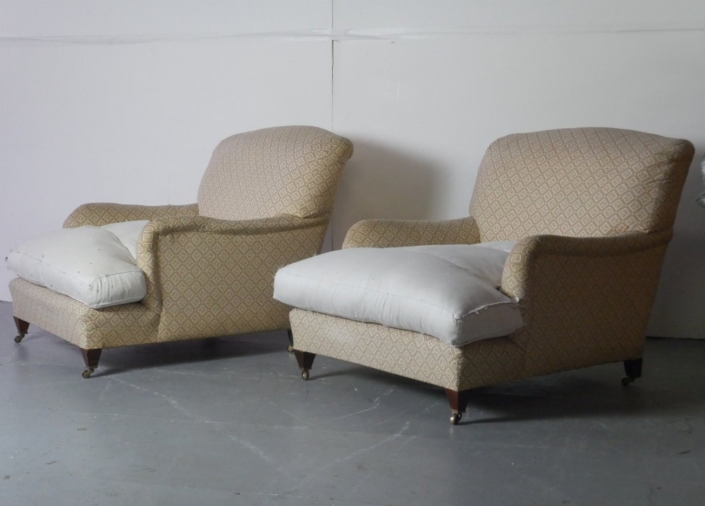 A pair of large upholstered armchairs in beige patterned fabric with deep white down cushions and brass castors on tapered timber feet.