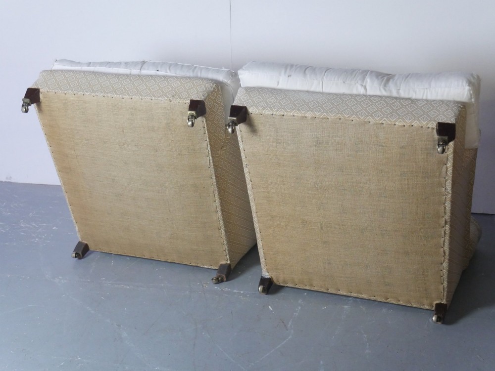 A pair of large upholstered armchairs in beige patterned fabric with deep white down cushions and brass castors on tapered timber feet. View VIII
