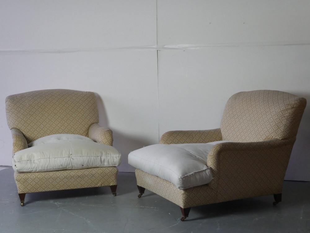 A pair of large upholstered armchairs in beige patterned fabric with deep white down cushions and brass castors on tapered timber feet. View X