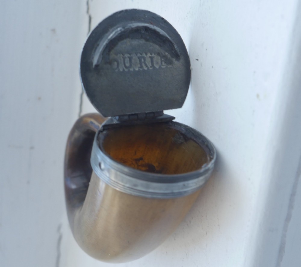 A curved brown horn snuff mull with a fitted metal rim and lid resting on a light surface. View III