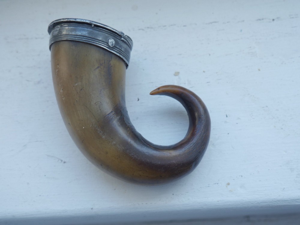 A curved brown horn snuff mull with a fitted metal rim and lid resting on a light surface. View IV
