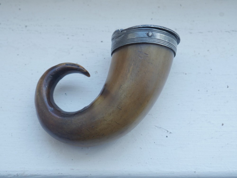 A curved brown horn snuff mull with a fitted metal rim and lid resting on a light surface. View V
